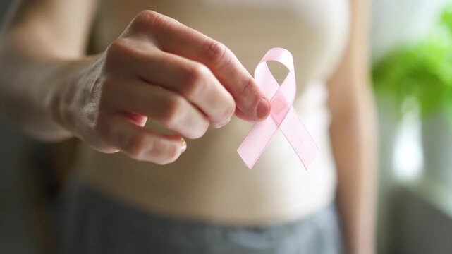 Close-up of female hand holding pink satin ribbon, symbolizing support for breast cancer awareness, medical care, and self-examination.