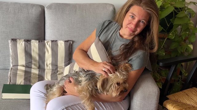 A serene woman sits on a sofa in a contemporary living room, calm and at leisure as she caresses her charming dog.