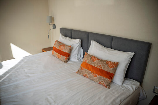 Modern luxury hotel bedroom interior with double bed, orange decorative runner, patterned pillows, large mirror, and warm sunlight. Cozy contemporary guest room design in resort or boutique hotel.