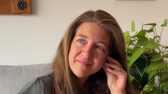 Mature woman enjoying a serene moment smiling and finding peace of mind while relaxing on a couch at home