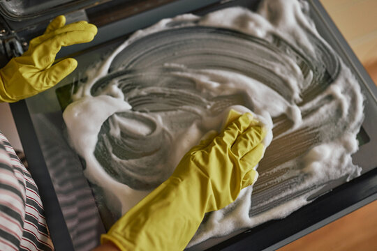 Person cleaning oven with sponge and soapy foam