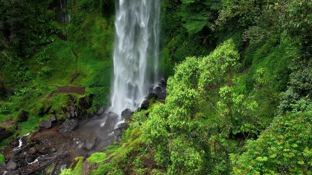 Aerial view of Waterfall Kayu Aro cascading down lush green cliffs surrounded by dense tropical vegetation in Kayu Aro, Jambi, Indonesia.