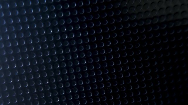 A dark patterned surface with rows of small circular bumps shifting diagonally.
