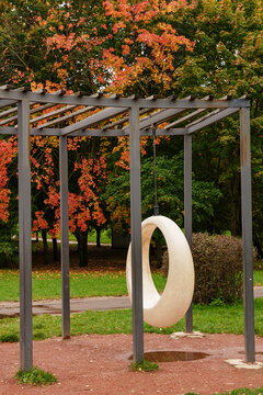 Ring swing hanging on metal pergola in autumn park. Urban space design, contemporary public infrastructure concept
