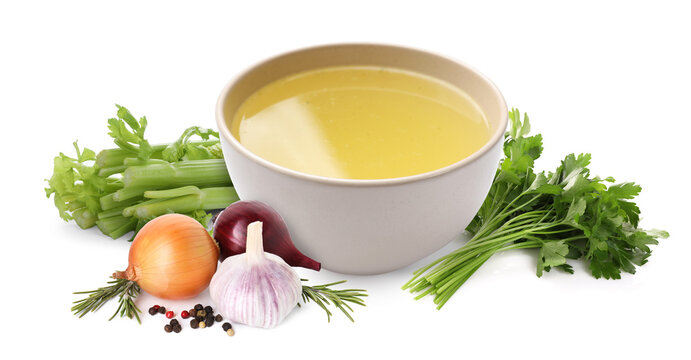 Broth in bowl, celery stalks, parsley, onion bulbs, rosemary, garlic and peppercorns on white background