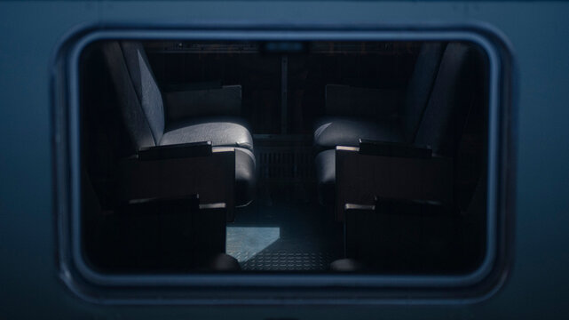 View through the window of a parked passenger train, featuring cool blue tones, reflections on the glass, and a softly blurred exterior scene. Railway transportation and travel concept.