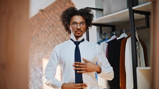 Young man tying necktie mirror home closet. Morning routine dressing work day.