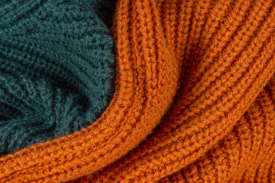 Macro shot of folded cozy knitted wool sweaters in warm orange and dark green colors. Abstract winter or autumn textile pattern background