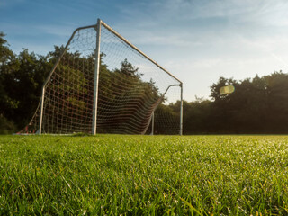 Fototapeta premium White soccer goal stands alone on green grass. Trees line the background under blue sky with wispy clouds. Scene peaceful and quiet, no people present. Ideal for sports, recreation