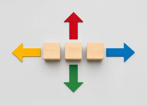 Wooden cubes surrounded by colorful arrows pointing in four different directions on a white background