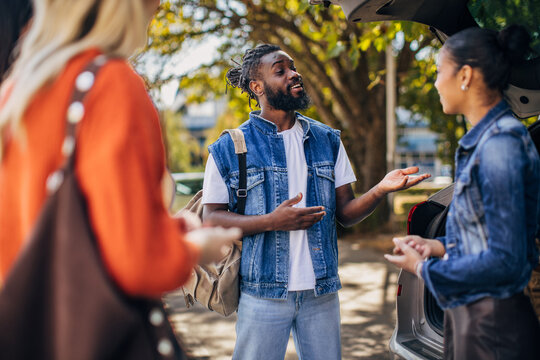 In a lively outdoor setting, diverse friends gather around a car, discussing plans for their upcoming road trip. The warm sunlight filters through the trees, creating a relaxed atmosphere as they shar