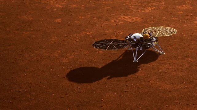 A lander is on the surface of Mars. It has a round body with two large, flat devices on top. Dust covers the reddish ground. The mission aims to study the planets environment.