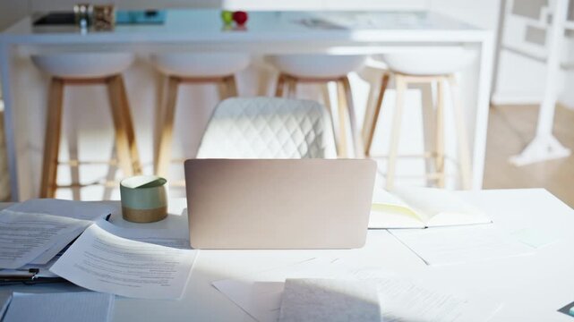 Laptop documents white desk sunny home kitchen. Remote work space no people.