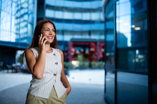 Happy businesswoman talking on phone outside modern office building