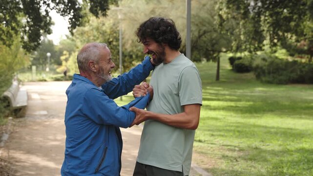 Portrait senior man and adult man hugging smiling after running sport training park. Intergenerational male friendship 