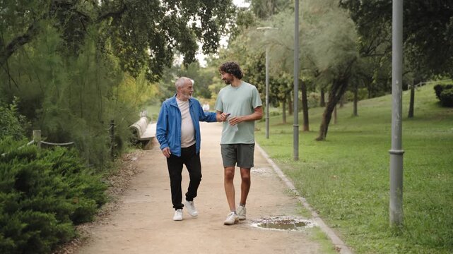 Adult son and elderly father walk together public park, enjoying conversation after practicing sport. Intergenerational relationships and care for older people. 