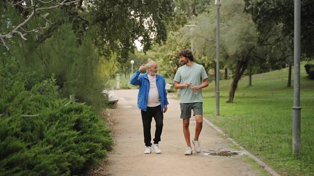 Senior father and adult son walking together wearing sportswear enjoying active healthy lifestyle park 