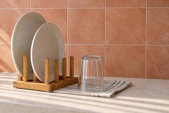 Ceramic plates in a wooden dish rack beside an inverted glass