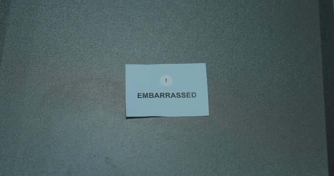 Embarrassed text on a white paper card against a gray background, representing awkwardness, selfconsciousness and emotional discomfort