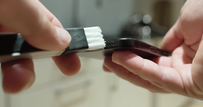 Close-up of a person cleaning the charging port of a smartphone with a small brush, representing phone maintenance, dust removal, device care and electronics cleaning.