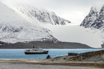 Fototapeta premium Remote summer Arctic landscape with ship, small cabin, blue fjord water and glacier framed by steep rugged mountains, Spitsbergen, Svalbard, Norway