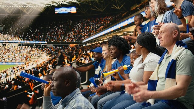 Young soccer fan cheers with blue supporters during a live match in a packed stadium as a family outing highlights fatherhood and shared sports experience.
