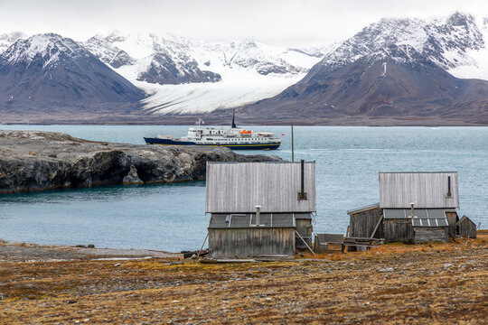 Historic wooden buildings of the abandoned Ny-London marble mining camp overlooking Kongsfjorden with ship and glacier scenery, Blomstrandhalvoya, Spitsbergen, Svalbard, Norway
