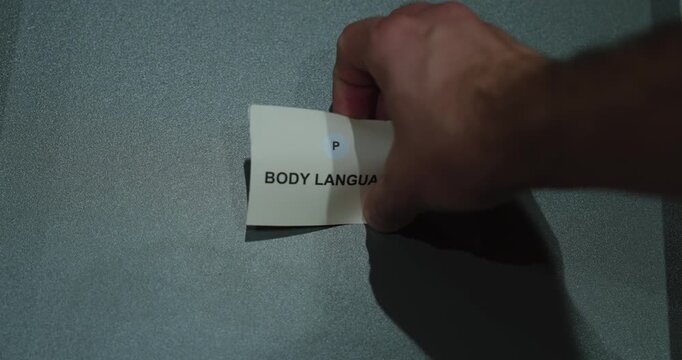 Hand holding a body language card against a gray background, representing nonverbal signals and communication skills