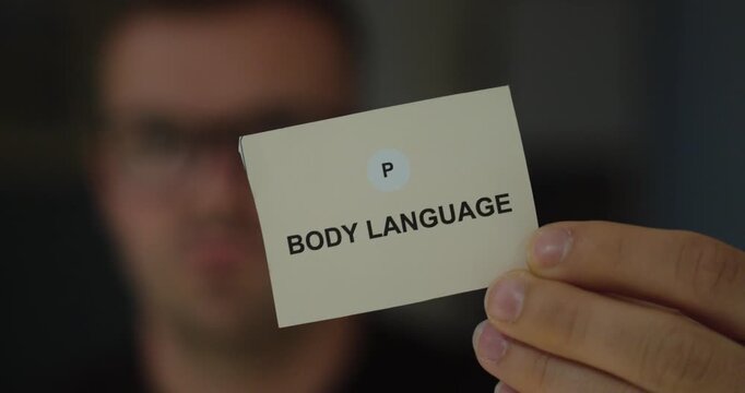Man holding a white card with body language text, representing nonverbal communication and interpersonal understanding