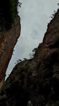 Low angle timelapse shot of grey clouds moving over steep rocky cliffs and vegetation of Presa de Isber canyon gorge in Alicante province, Spain
