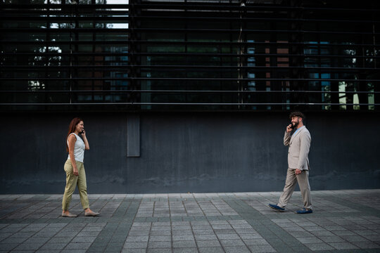 Man and woman walking, communicating on smartphones outdoors
