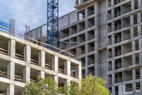 Tall multi-story residential building under construction with exposed concrete structure and blue crane