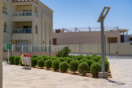 Modern resort complex with clean pathways, manicured green bushes, and contemporary architecture under clear blue sky.