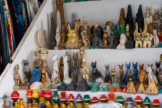 Collection of Egyptian souvenir figurines, statues, and obelisks displayed on shelves inside souvenir shop.