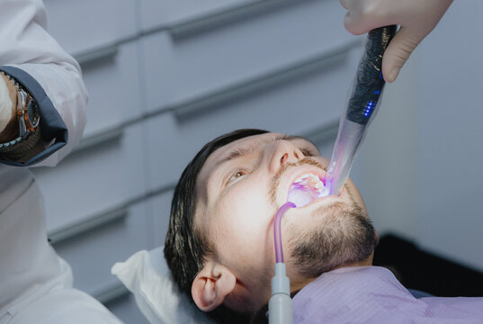 A dental assistant treats a young patient's molar with a polymerization lamp in a clinic.
