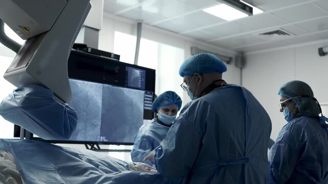 Medical team analyzing angiographic images of blood vessels on a large monitor during an interventional procedure.