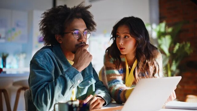 Diverse coworkers solving laptop problem. Man confused, woman explaining ideas.