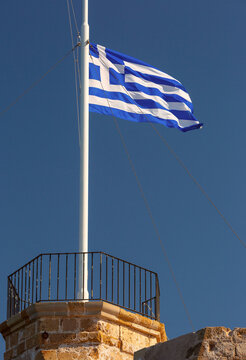 Greek national flag waving on a flagpole above the historic stone fortifications of Chania, Crete, Greece.