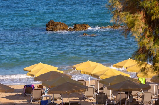 Sandy beach with sun loungers and yellow umbrellas beside the turquoise Mediterranean Sea on the island of Crete, Greece.