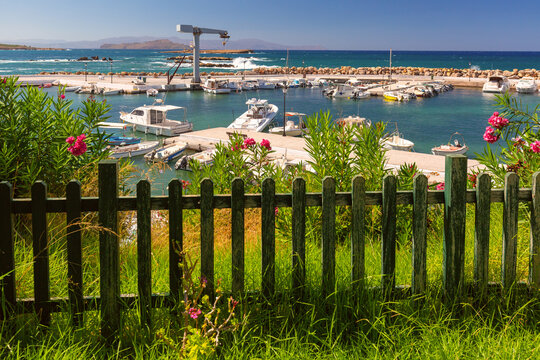 Small coastal marina with moored boats, flowering oleanders and turquoise Mediterranean Sea in Chania, Crete, Greece.