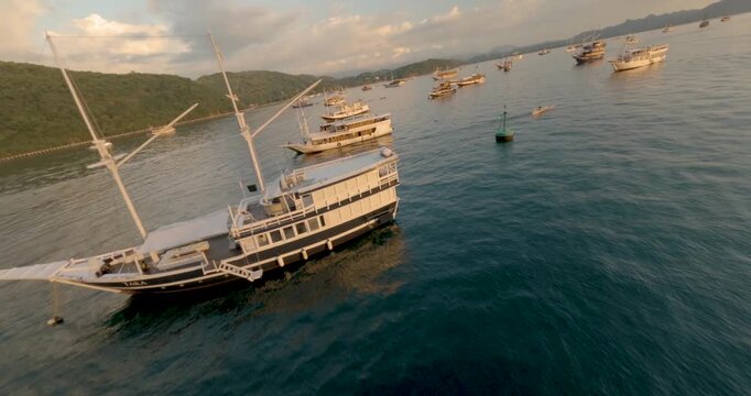 FPV aerial view of traditional phinisi boats anchored in the calm blue waters of Labuan Bajo bay in Komodo, East Nusa Tenggara, Indonesia.