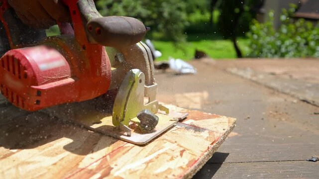 Roofer cutting a wooden board with a circular saw during roof construction and repair work.