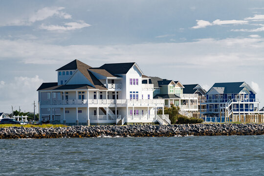 A waterfront house with broad porches stands above the rocky Hatteras shoreline.