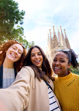 Vertical. Young only women friends taking selfie in front of Sagrada Familia, Barcelona. Beautiful mixed race girl on street of European city enjoying vacation happy and smiling. Funny tourism people