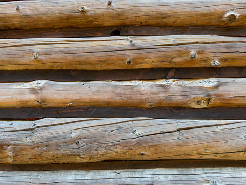 Horizontal background texture of stacked wooden logs. Weathered timber beams with natural knots and cracks form a textured wall of a traditional log structure.