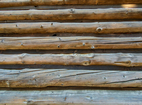 Close up texture of horizontal wooden logs. Parallel stacked wooden logs with natural grain and knots form a rustic surface with dark gaps between them.