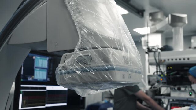 Close-up of a C-arm angiography system covered with a sterile protective drape in a modern cath lab.