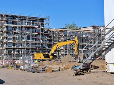 Yellow Excavator Working at Modern Building Construction Site with Scaffolding Under Clear Blue Sky for Urban Infrastructure Development Project