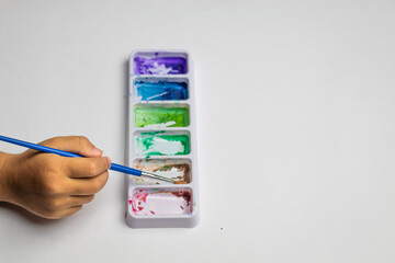 Child's hand dips brush into watercolor palette © Muhammad Azhar