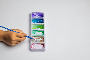Child's hand dips brush into watercolor palette © Muhammad Azhar